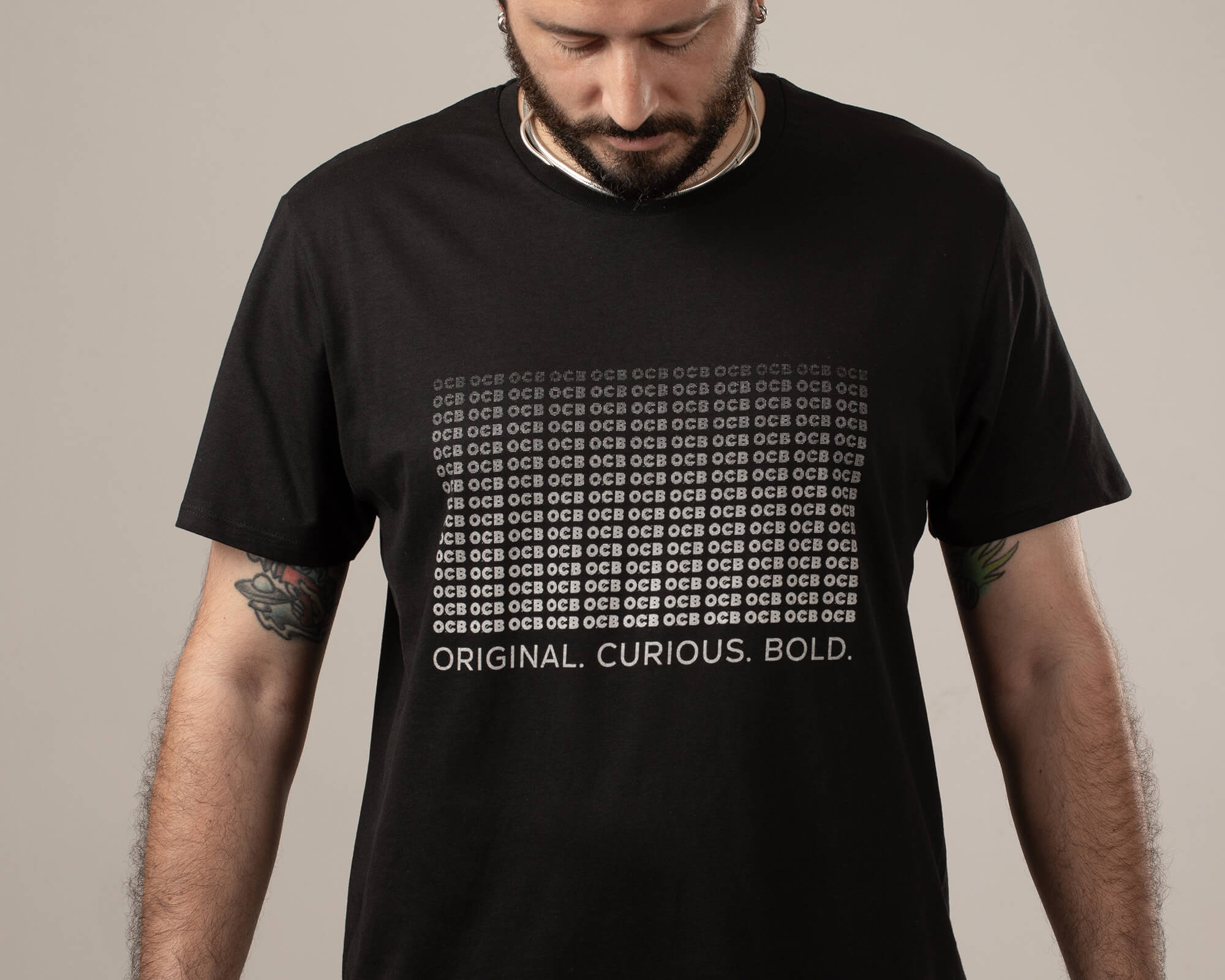 A person wearing a black OCB t-shirt with white text that reads 'ORIGINAL, CURIOUS, BOLD.'