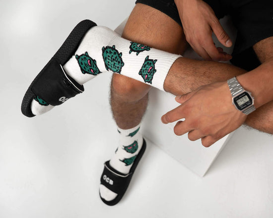 Person wearing white socks with green designs and black flip flops on a white background
